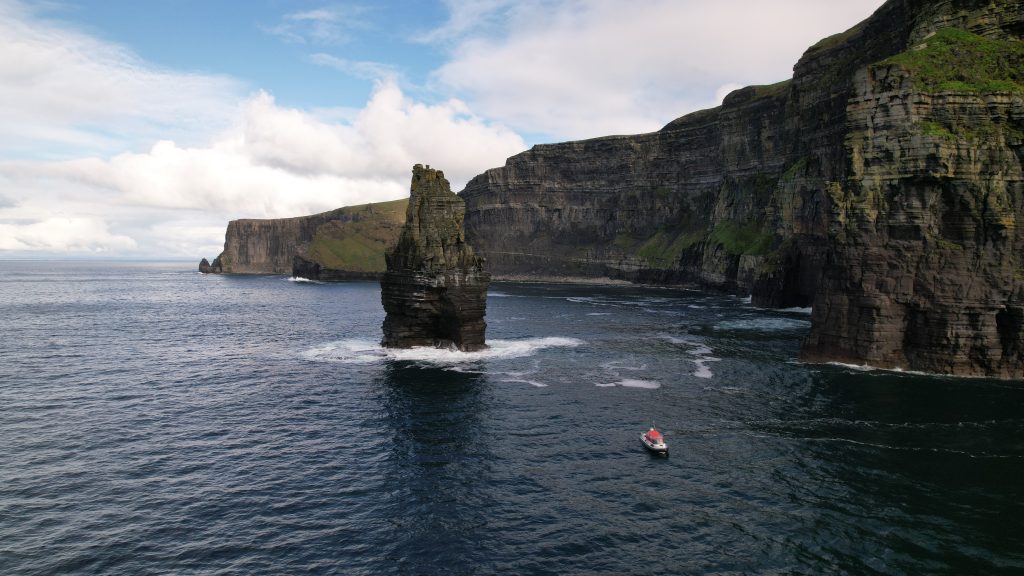 Doolin ferry passing the Cliffs of Moher and sea stacks in County Clare, Ireland.