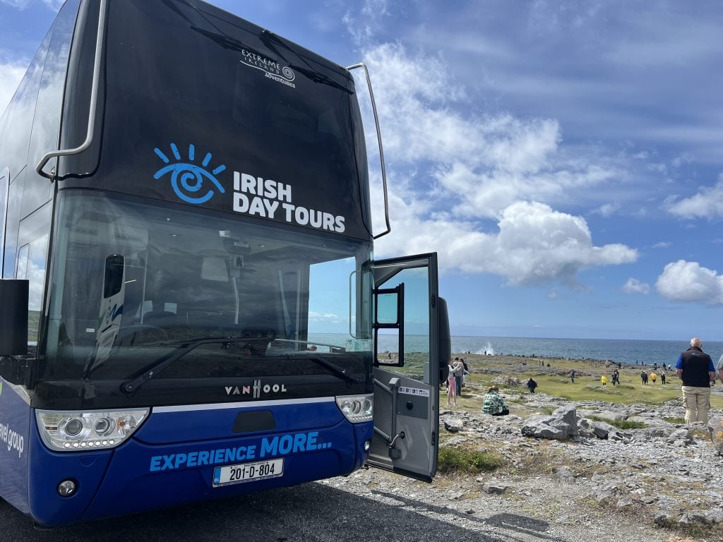 An Irish day tour bus parked at a scenic location with mountains and greenery.